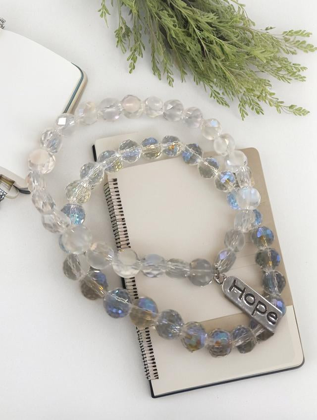 House of Joy Beaded bracelet with 'hope' charm on a notebook with greenery in the background
